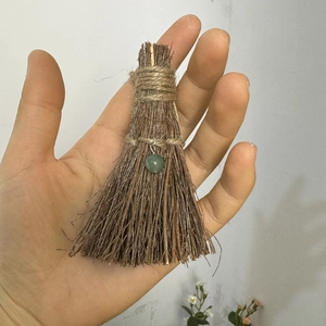 Detailed close-up of a mini handmade broom with natural wood sticks and green bead charm