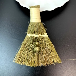 Detail showing a handmade decorative straw broom with a vintage bronze bee pendant detail