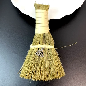 Detail of a handmade straw witch broom with a silver Triquetra charm on dark background