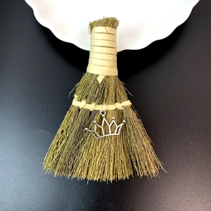 Detailed close-up of handmade mini broom with straw fibers and a silver crown pendant