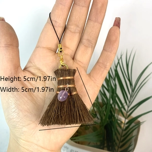 Mini natural fiber broom pendant with bronze wire and purple stone held in hand