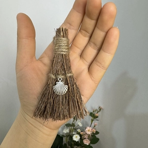 Macro detail of a handmade mini broom keychain with shell pendant held in hand