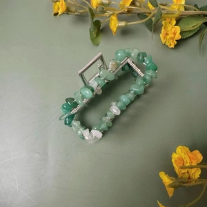 Détail d'une pince à cheveux argentée avec pierres de cristal vert sur fond floral naturel