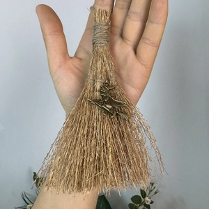 Close-up of handmade mini witch broom with bronze charm and natural straw texture