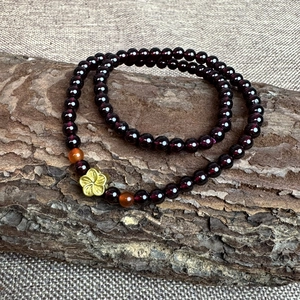 Double-wrap garnet and red agate beaded bracelet featuring a gold flower pendant on bark