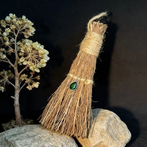 Close-up of green teardrop gemstone pendant hanging on a decorative straw broom