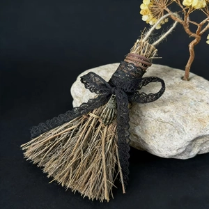 Detail of handmade broom with black lace bow and vintage metal skull hand charm
