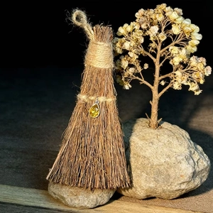 Detail shot of mini straw broom with yellow crystal pendant on natural stone base