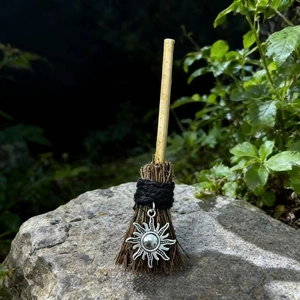 Miniature handmade witch broom with silver sun charm on a forest rock for Halloween decor