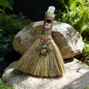 Detail of handcrafted mini witch broom with natural straw, crystals and a brass bee charm