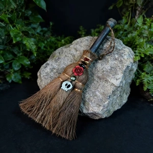 Detail of handcrafted witch broom with skull charm and rose on a natural rock background