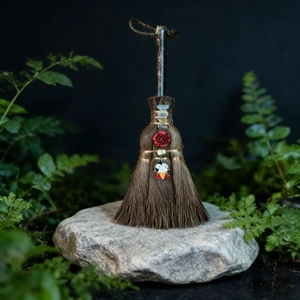 Detail of a handmade witch broom with crystals, red rose, and a vampire charm ornament