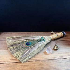 Détail d'un balai d'autel artisanal avec plumes de paon, cristaux et pendentif dragon