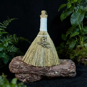 Close-up of handmade witch broom with natural straw, white rope, and bronze pendant