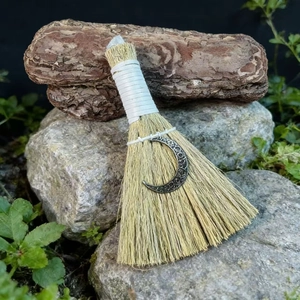 Detail of a handmade witch altar broom with natural grass, crystal, and moon charm