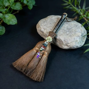 Detail of a handmade witch besom with metal rose, natural stones and purple charm