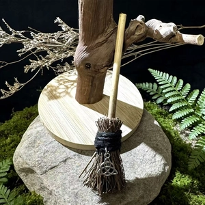Macro detail of a handmade mini witch broom with natural wood and a silver triquetra charm