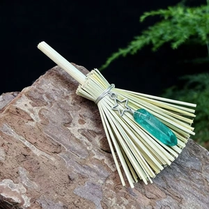 Macro detail of witch broom ornament with green crystal and silver pentagram on a rock