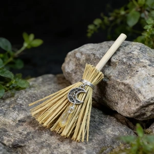 Detail of mini witch broom with silver moon pendant and crystal on natural rock