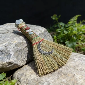 Detail of a handmade wicca altar broom with natural stones and crescent moon charm on a rock