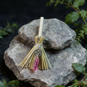 Detail of mini witch broom with pentagram charm and pink crystal on gray stone background