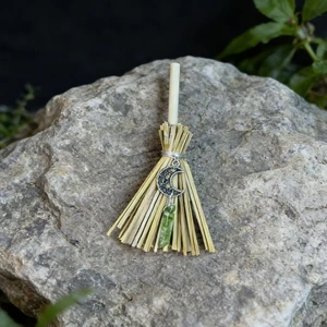 Macro shot of mini witch broom with crescent moon charm and green raw crystal on grey stone