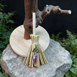Detail of a handmade witch broom with a Celtic knot and a purple crystal pendant