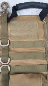Detail of tan tactical gear featuring MOLLE webbing, D-ring, and ergonomic rubber handle