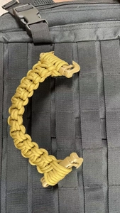 Tactical coyote brown paracord handle with dual buckles attached to a black MOLLE backpack