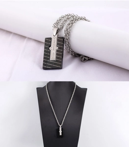 Macro detail of men's black stainless steel rectangular pendant with silver cross and engraving