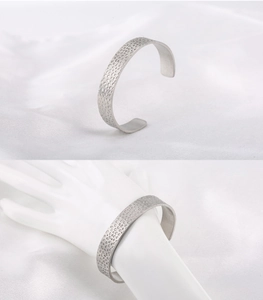 Détail du bracelet manchette en acier argenté avec texture martelée sur soie blanche
