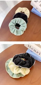 Detail of ribbed knit scrunchies in black, mint green, and beige colors on wood surface