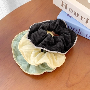 Pastel knit corduroy scrunchies in black, yellow and green on a wooden background