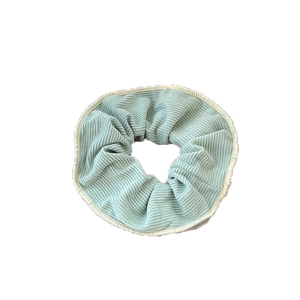 Mint green corduroy scrunchie with white stitching on minimalist white background