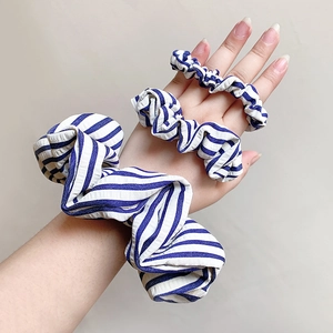 Three sizes of blue and white striped seersucker scrunchies worn on a hand for scale