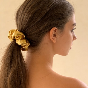 Close-up of golden metallic scrunchie with shiny pleated texture on a ponytail