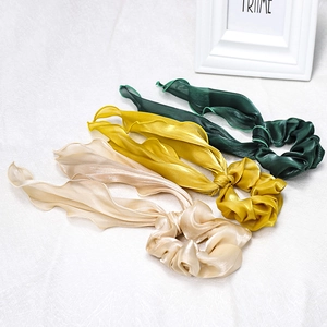 Detailed view of three satin ribbon hair scrunchies in green, yellow, and beige colors