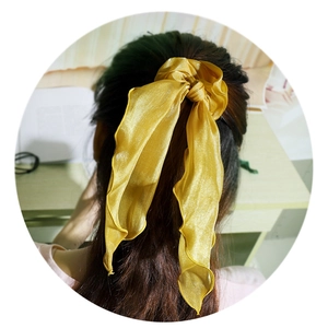 Detailed view of a golden satin ribbon hair tie styled on a sleek low ponytail
