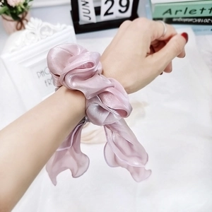 Detail of light pink satin scrunchie with long ribbons worn on wrist with soft sheen