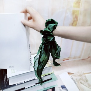 Detailed texture of dark green silk satin hair scrunchie with long ribbon and wavy edges