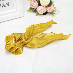 Close-up of elegant bright golden silk satin ribbon scrunchie with soft pleated texture