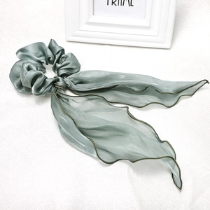 Detail view of large sage green satin bow scrunchie with long wavy ribbons and silky texture