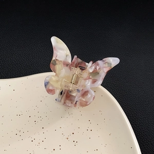 Elegant butterfly hair claw clip in marble-patterned acetate on a ceramic tray