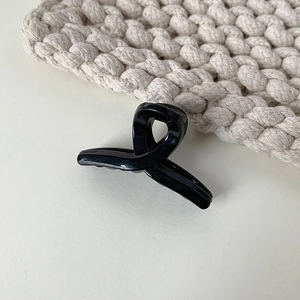 Detailed view of a sleek black twisted ribbon hair claw clip on a neutral textured surface