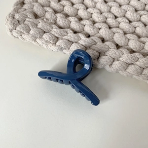 Close-up of a glossy navy blue mini hair claw clip with a stylish cross-knotted design