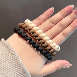 Three-piece spiral telephone cord hair ties in black brown and cream on a wrist