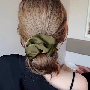 Détail d'un chouchou en satin vert foncé sur un chignon bas montrant la texture soie