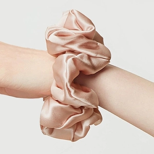 Chouchou en satin rose champagne au fini brillant porté au poignet d'un modèle