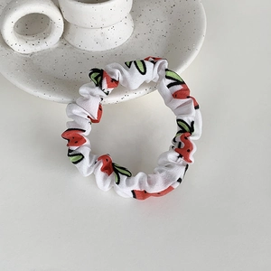 Détail d'un chouchou en tissu blanc avec motifs de cerises rouges sur un plateau chic