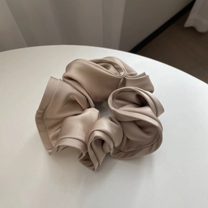 Detailed view of large champagne silk scrunchie with ruffled edges on a white table